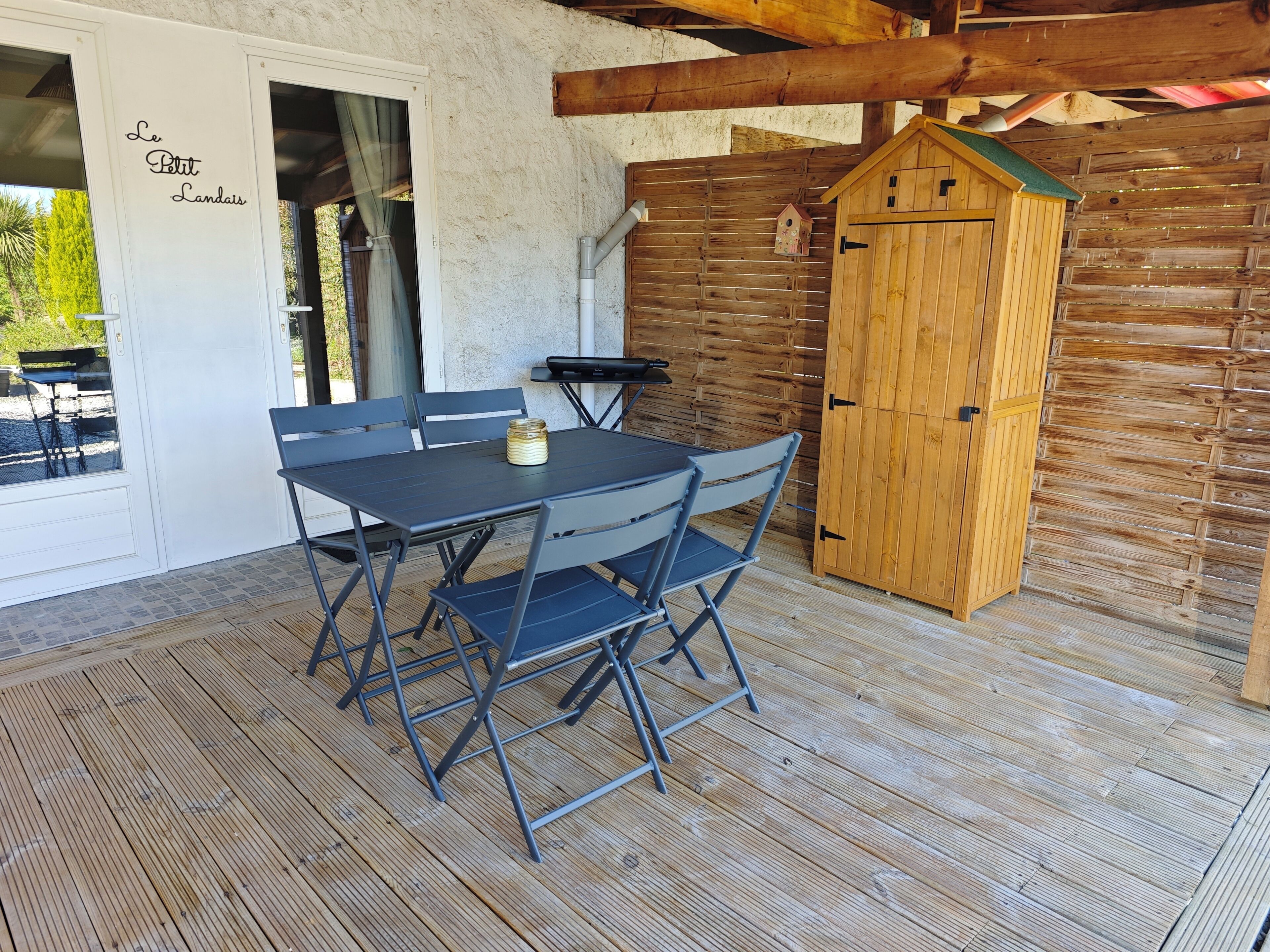 A patio with a table and chairs, a wooden cabinet, and a door with 'Le Petit Landais' text.