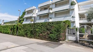 Un edifici residencial de diversos pisos amb balcons, entrada tancada per reixa i una tanca de boix.