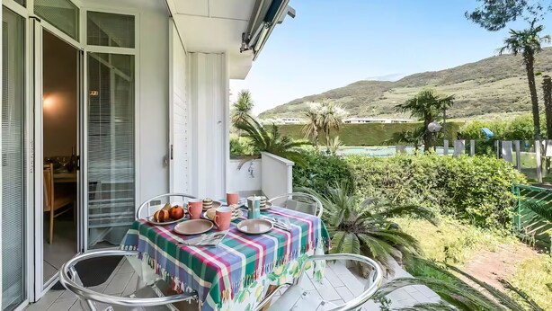 Un balcón con una mesa lista para comer, una puerta corrediza de vidrio y vistas a un paisaje montañoso.