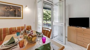Un área de comedor con una mesa dispuesta para dos personas, un televisor y vistas a través de un ventanal.