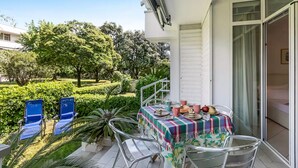 Un balcó amb taula preparada per dinar, caires i vista a un jardí.