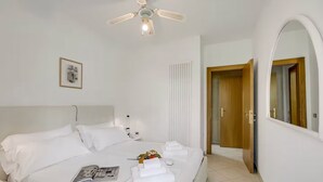 Una habitación de hotel con una cama, un ventilador de techo, un espejo, una puerta y un cuadro en la pared.