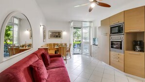 Una cocina moderna con horno y microondas integrados, una zona de comedor con mesa y sillas, y un sofá rojo.