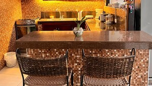 A kitchen with a tiled backsplash, dark wooden cabinets, a central island with chairs, and a hanging decorative item.