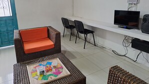 A room with a wicker sofa, two black chairs, a television, and a board game on a tray.