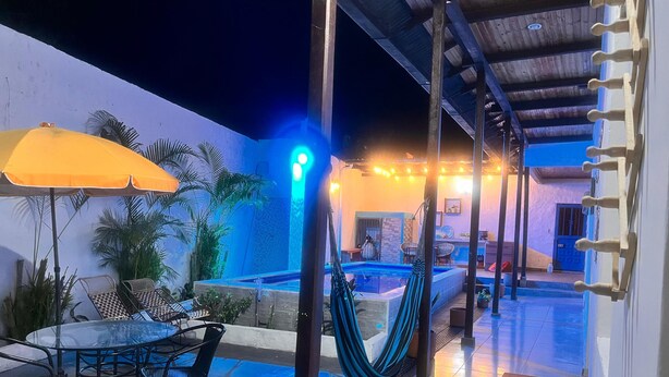 A pool area with a table and chairs, a hammock, and a blue-lit pool.