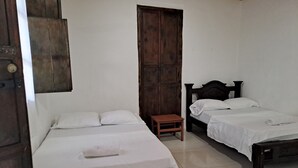 A room with two beds, a wooden door, and a small table.