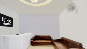 A reception area with a white reception desk, a brown leather sofa, and a wall-mounted fan.