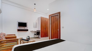 A hotel room with a bed, a TV, a wardrobe, a desk with a kettle, and a coffee machine.