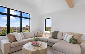 Una sala de estar moderna con un sofá modular, una mesa de centro redonda y grandes ventanas con vistas al vecindario.