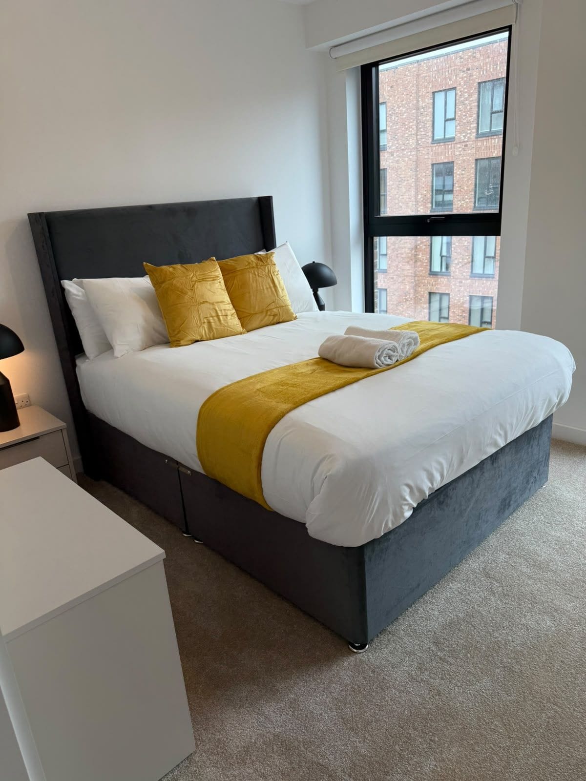 Habitación de hotel moderna con una cama grande, vista a un edificio de ladrillo y una ventana.