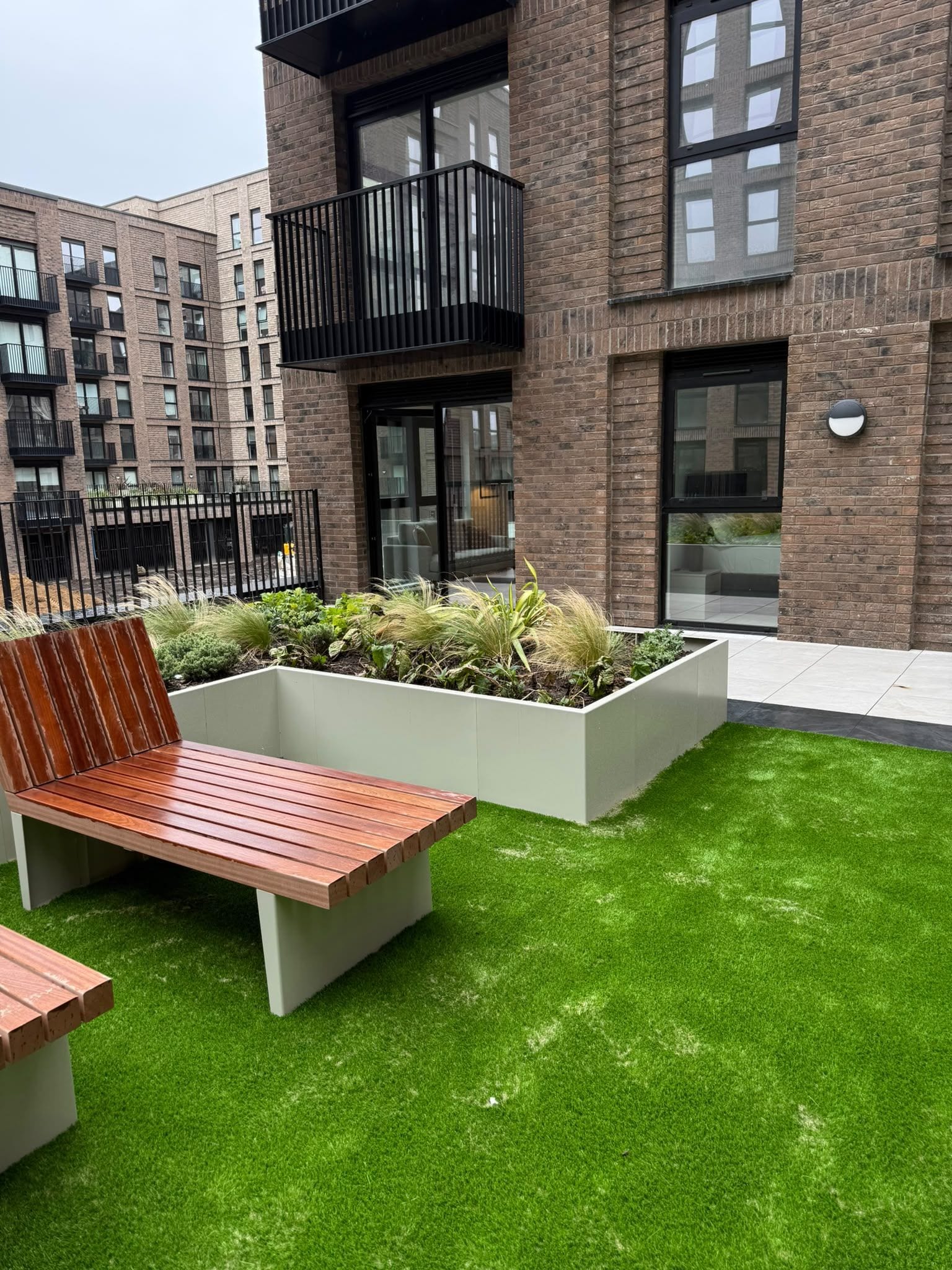 A modern outdoor seating area with a bench and planters, adjacent to a building with brick facade and large windows.