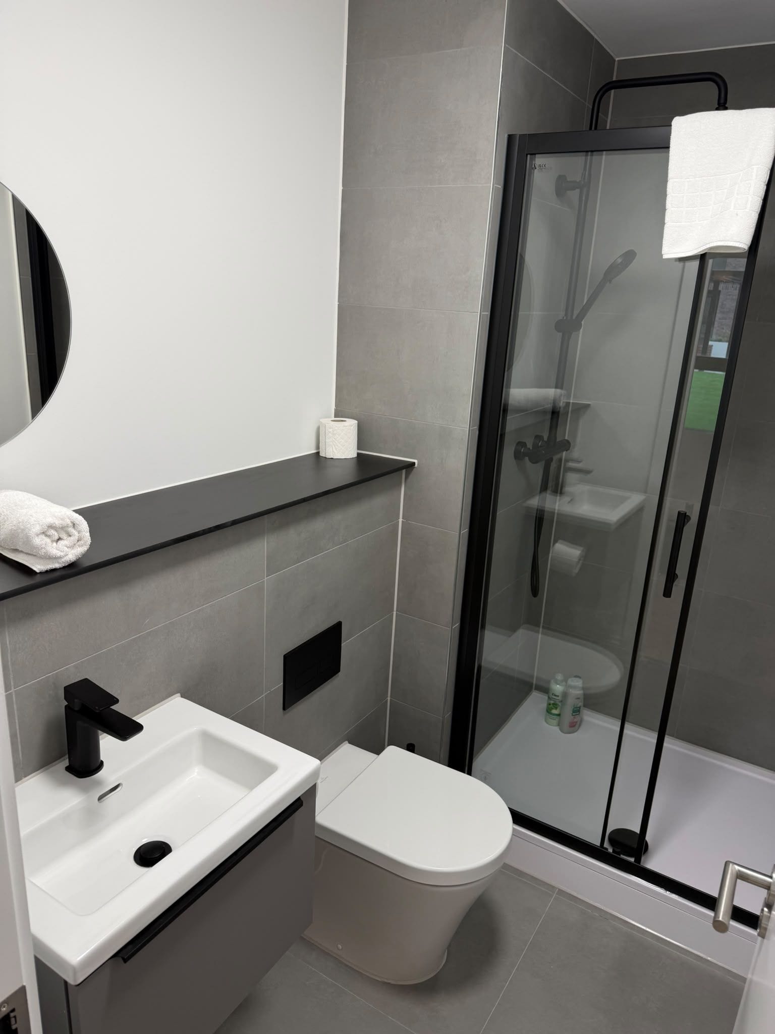 A modern bathroom with a glass shower enclosure, a white toilet, a sink with a black faucet, and a towel on the countertop.