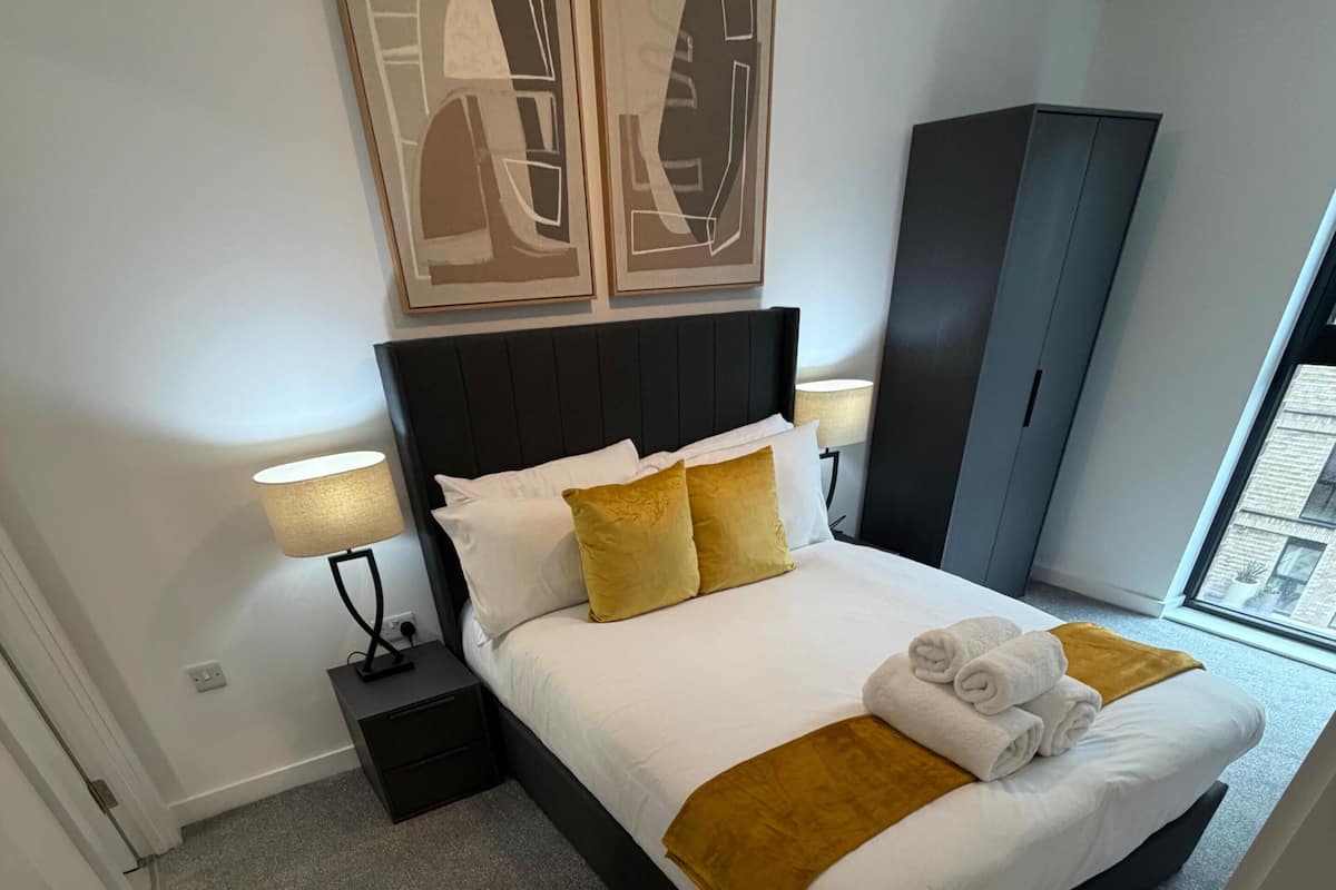 A neatly arranged hotel room with a bed, a wardrobe, a nightstand, a lamp, and a window.