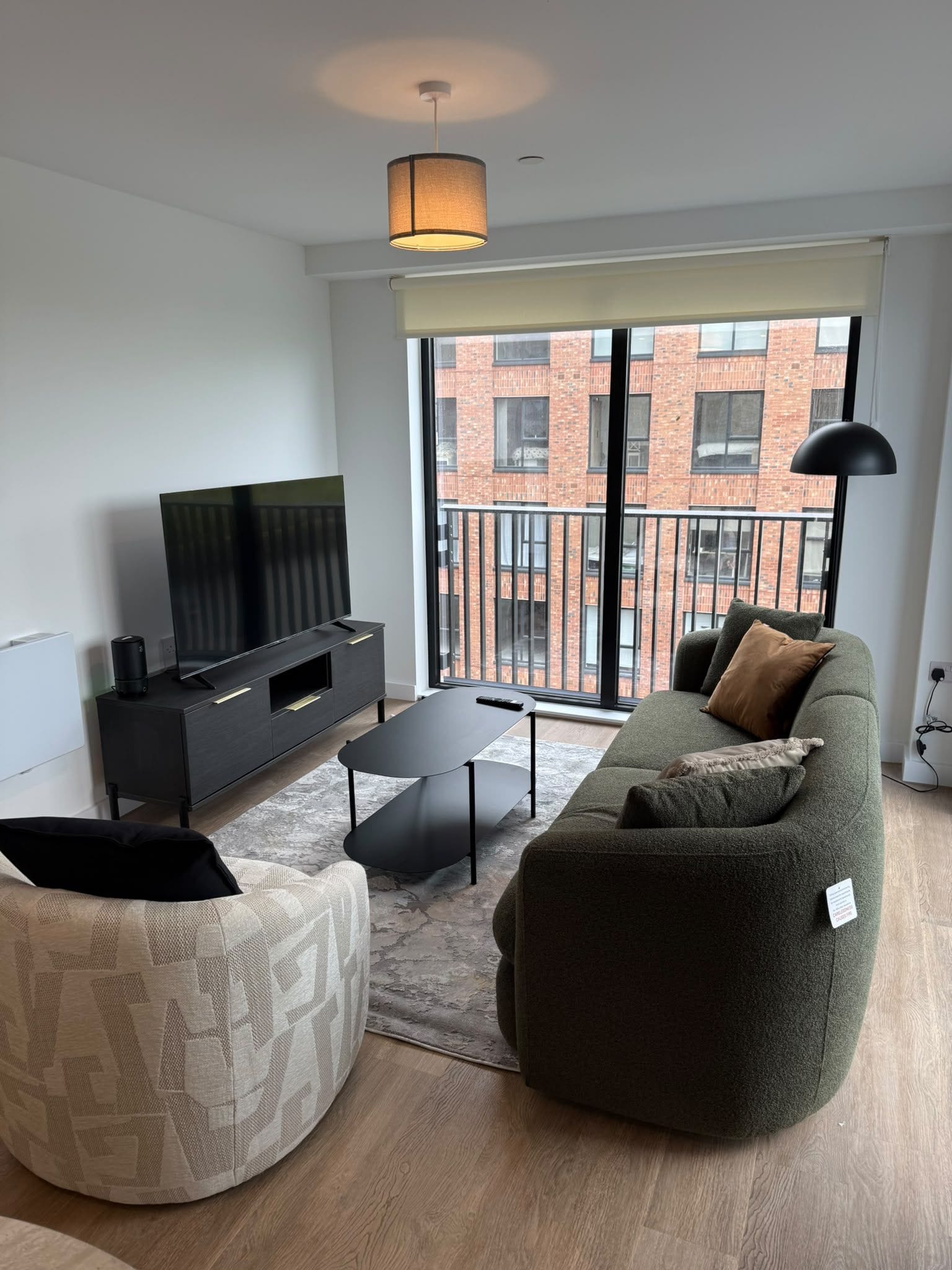 A modern living room with a sofa, a coffee table, a flat-screen TV, and a large window with a view of a brick building.