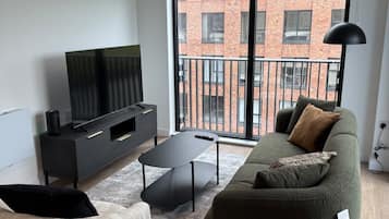 A modern living room with a sofa, a coffee table, a flat-screen TV, and a large window with a view of a brick building.