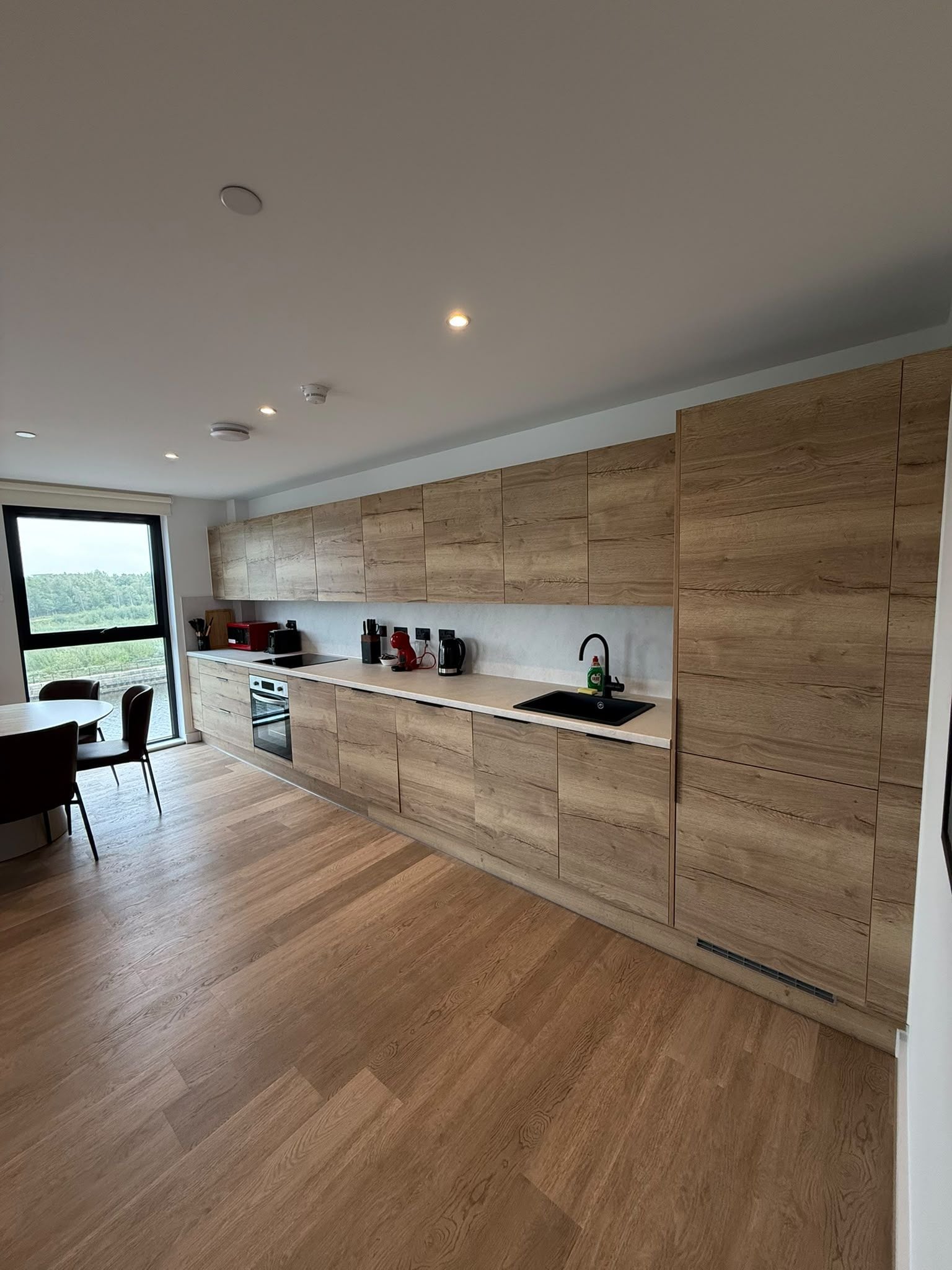 Una cocina moderna con armarios de madera, un lavamanos negro y un comedor con mesa y sillas.