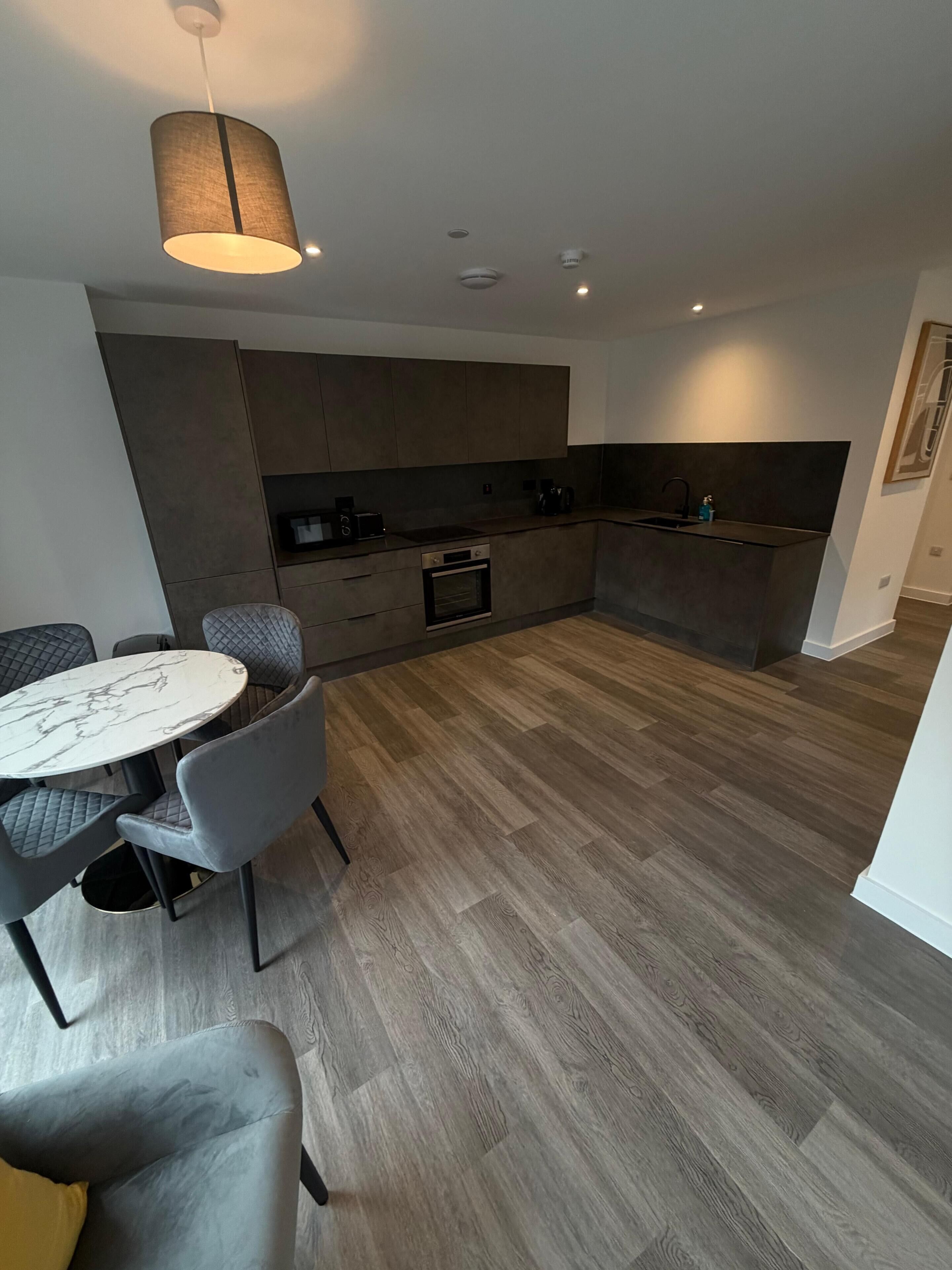 Una cocina moderna con electrodomésticos integrados, una zona de comedor con una mesa de mármol y una silla tapizada en gris.