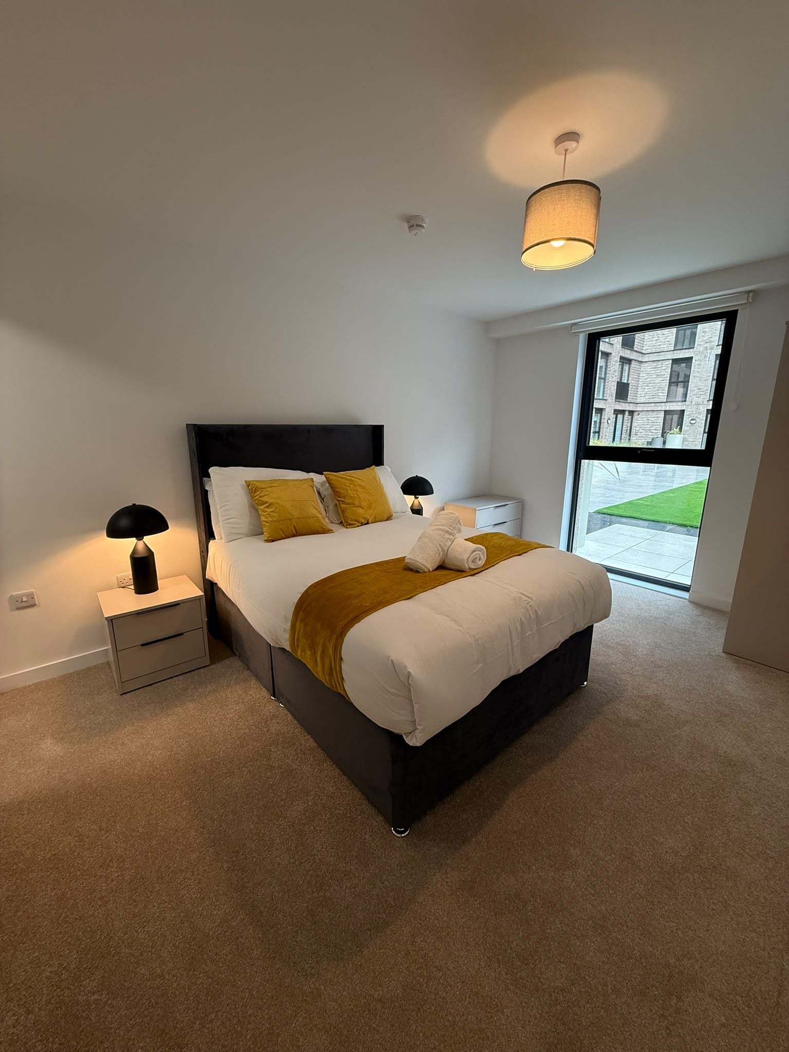 A modern bedroom with a bed, bedside tables, a lamp, and a view of the outside.