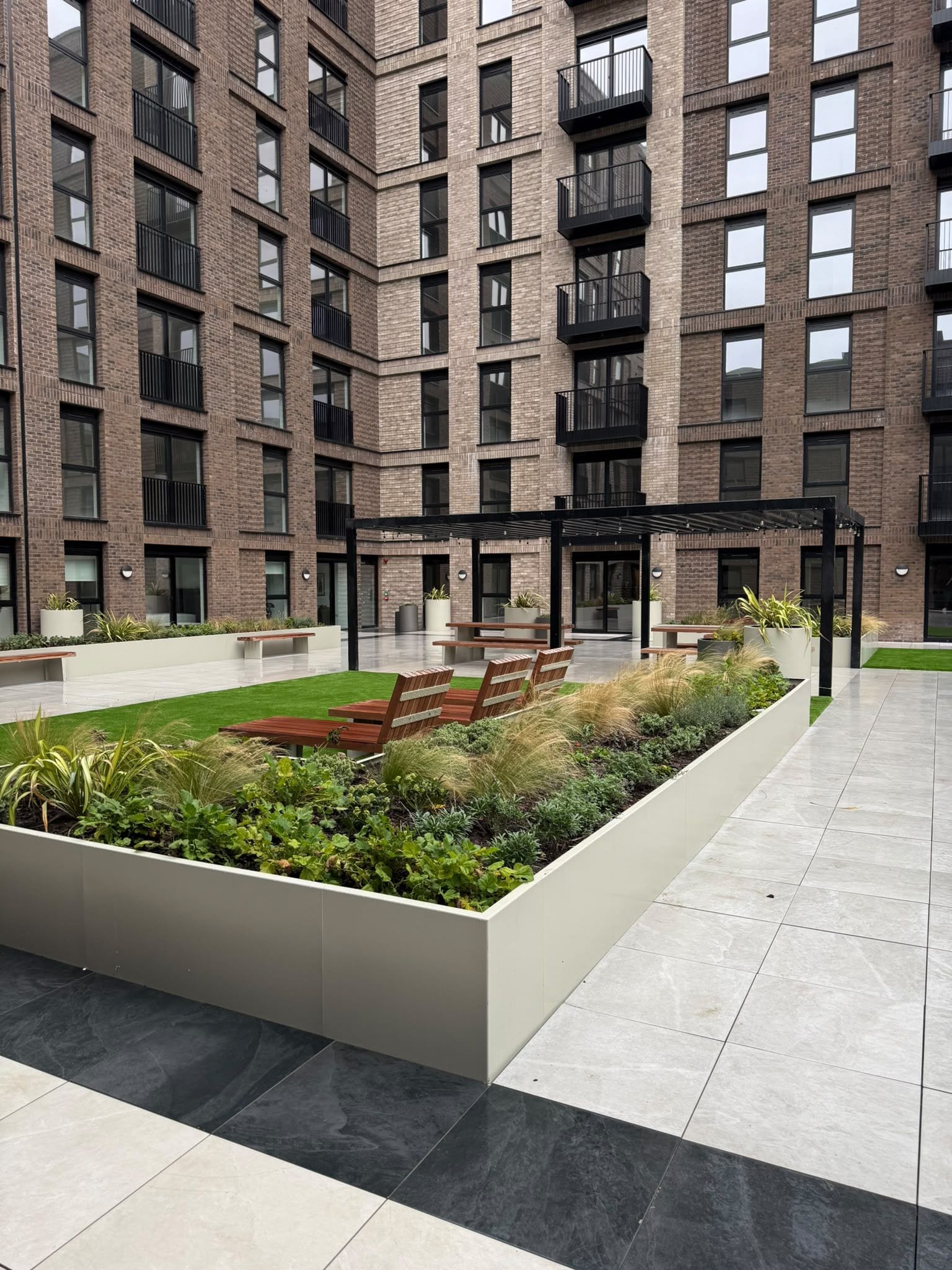 Un edificio de varios pisos con un patio central que cuenta con una zona de estar, jardineras y una pérgola.