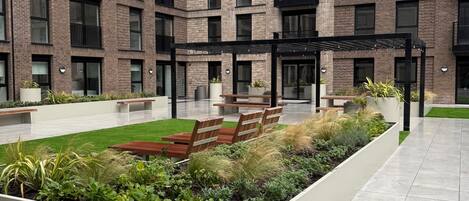 Un edificio de varios pisos con un patio central que cuenta con una zona de estar, jardineras y una pérgola.