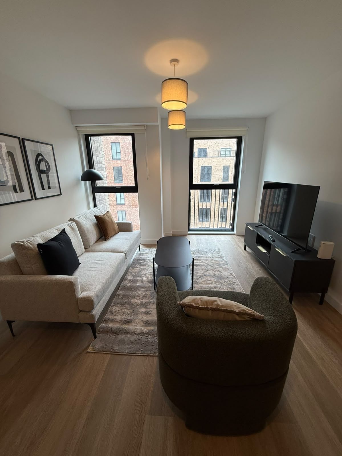Una sala de estar moderna con un sofá, sillón, televisor y un amplio ventanal con vista a la ciudad.