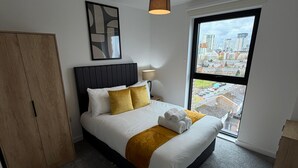 Ett modernt hotellrum med en stor säng, en garderob, utsikt över staden genom fönstret och en taklampa.
