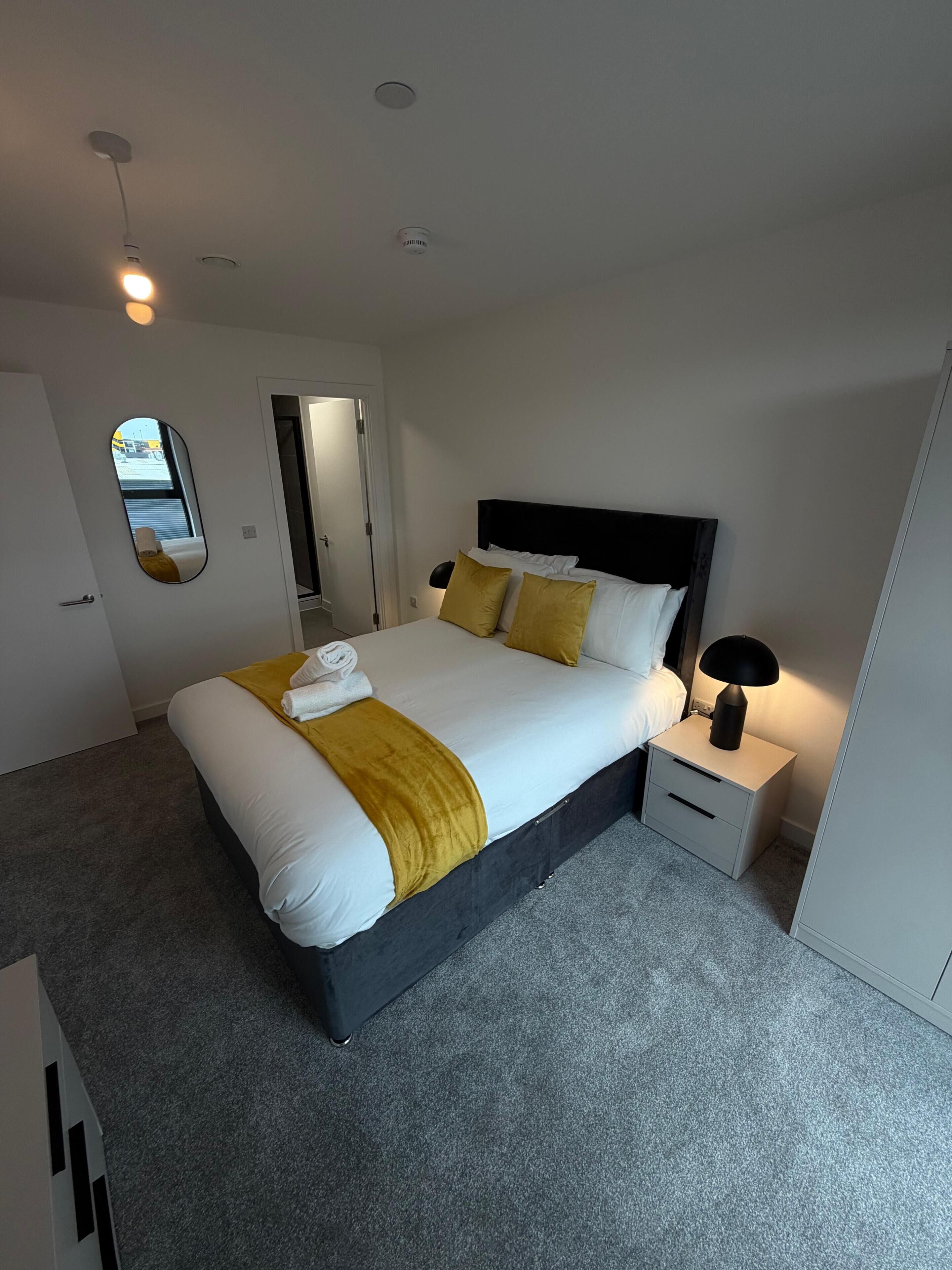 A modern bedroom with a bed, bedside tables, a mirror, and a door.