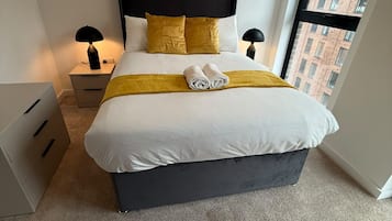 Habitación de hotel moderna con una cama grande, dos mesitas de noche, un ventanal con vistas a la ciudad y suelo alfombrado.