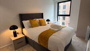 A modern bedroom with a large bed, bedside lamps, a window with a view of buildings, and a ceiling light.
