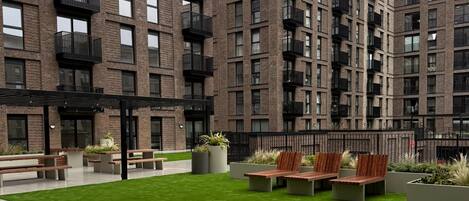 Ein modernes Apartmenthaus mit mehreren Balkonen, einem Innenhof mit Sitzgelegenheiten und einem gepflegten Rasen.