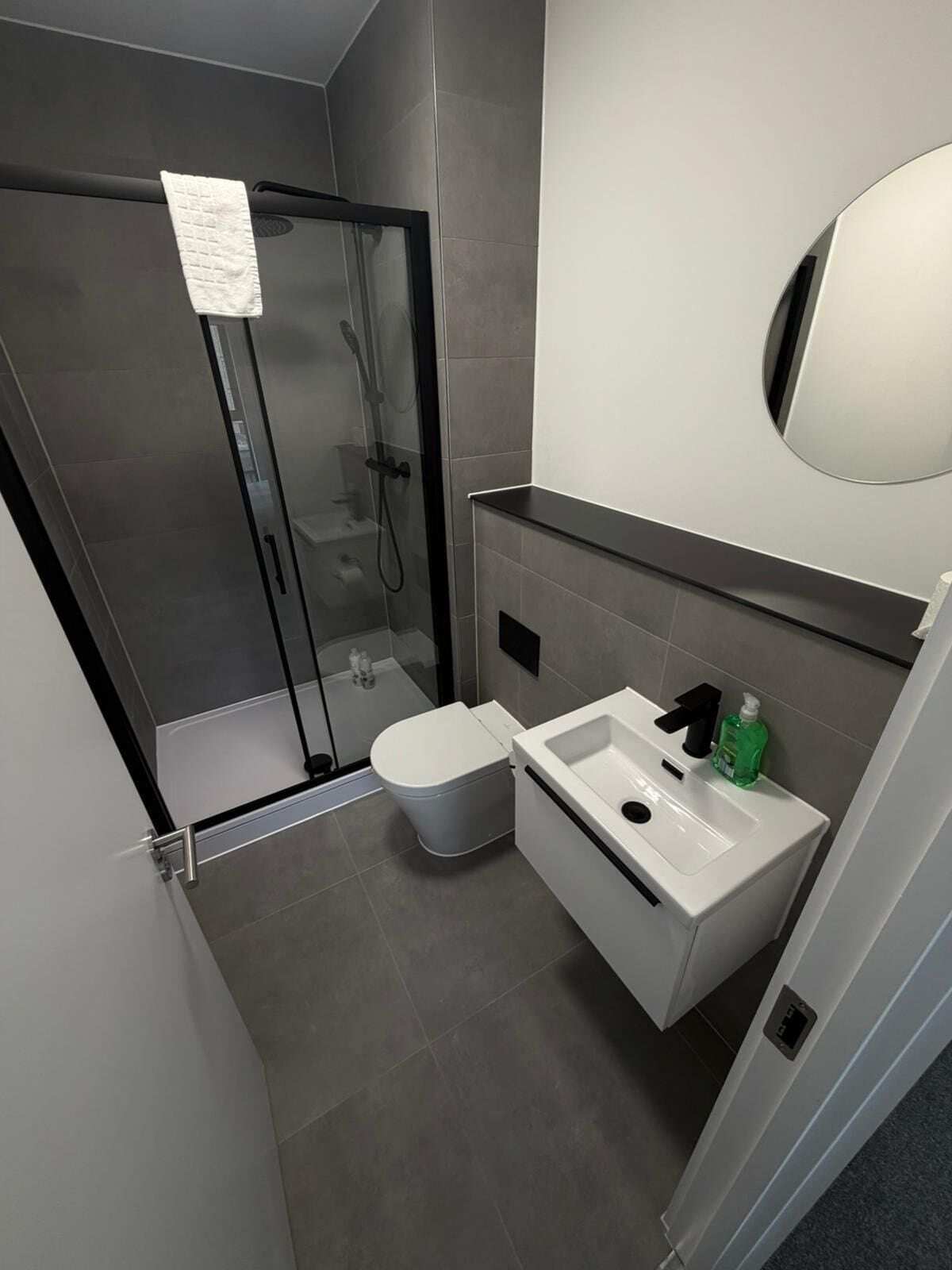 Un baño moderno con cabina de ducha de vidrio, inodoro blanco y lavamanos blanco con espejo superior.