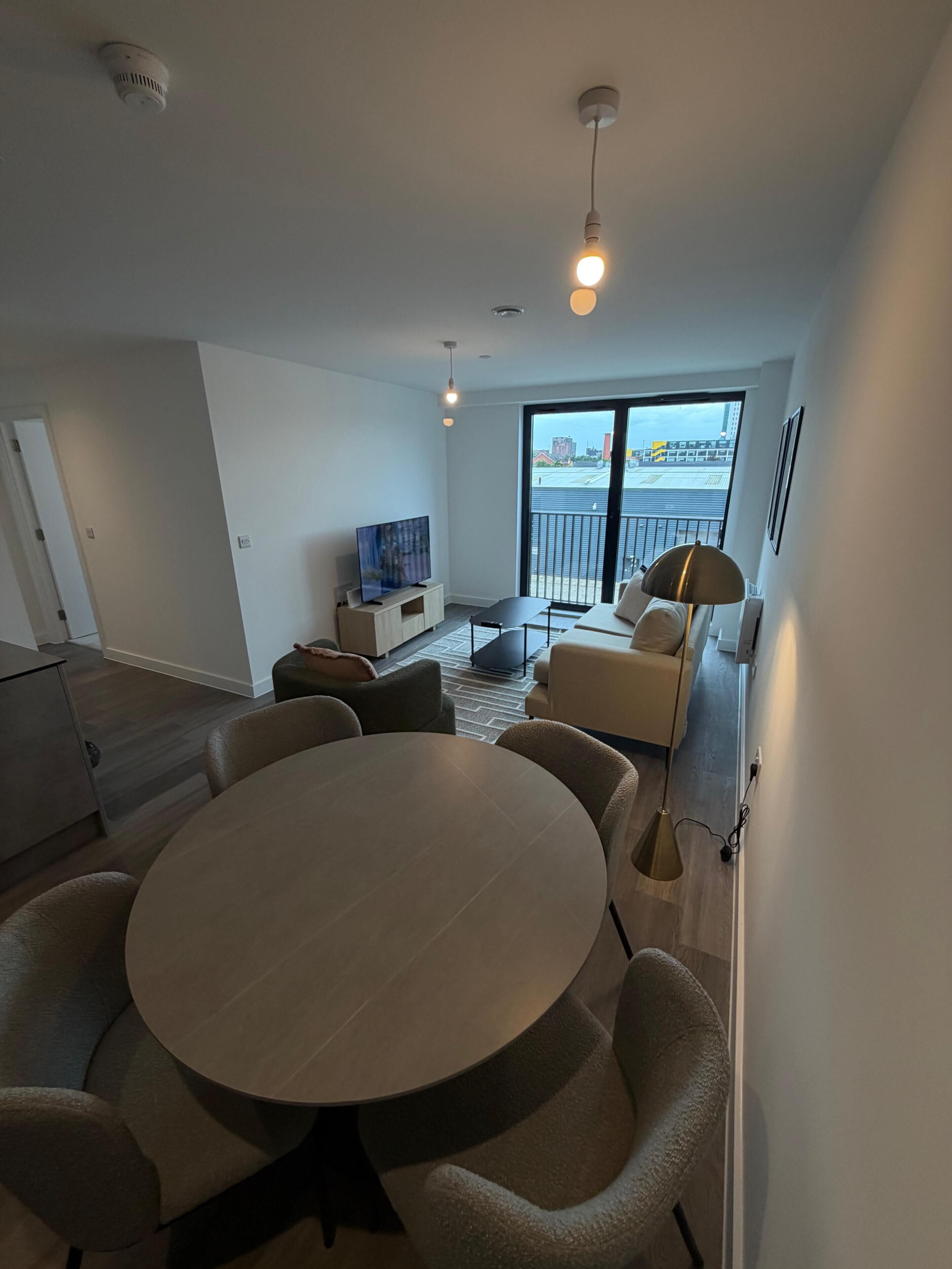 A modern living room with a round table, sofas, a TV, and a large window with a view.