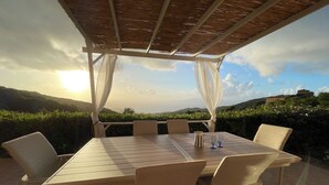 Ein Essbereich im Freien mit Tisch und Stühlen, einer Pergola darüber und einem schönen Ausblick auf Hügel und ein Gebäude in der Ferne.