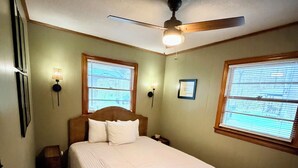 Un dormitorio con una cama, dos lámparas de pared, un ventilador de techo y dos ventanas con persianas.