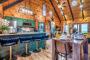 L’intérieur d’un chalet en bois comprend une cuisine, un coin repas, des tabourets de bar et une grande fenêtre.