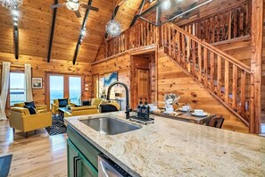 Interior de una cabaña de madera con cocina, comedor y una escalera.