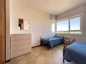 A bedroom with a bed, a dresser, a window, and a mirror. - Seafront Apartment on the Promenade (Lignano Sabbiadoro)