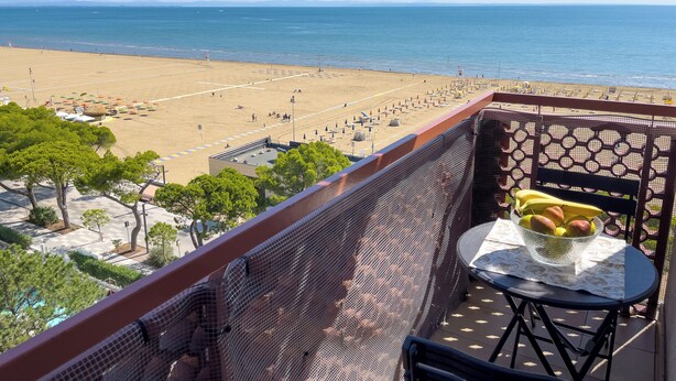 Ein Balkon mit Blick auf einen Strand, ein Tisch mit einer Obstkorb und ein Stuhl.
