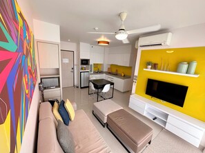 A modern living room with a sofa, ottoman, and a flat-screen TV mounted on a yellow wall. - Cassia 2 BR water (Choeng Thale)
