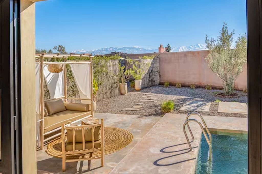 Un área de piscina con una silla de descanso y una mesa pequeña, rodeada por un jardín con vistas a las montañas.