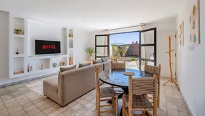 Een moderne woonkamer met een flatscreen-tv, een bank, een eettafel met stoelen en een groot raam met uitzicht.