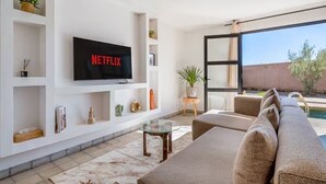 Een moderne woonkamer met een flatscreen televisie, een bank, een glazen salontafel en uitzicht op een zwembad.