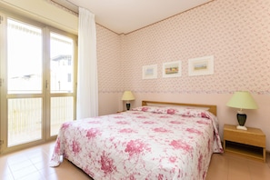 Ein Schlafzimmer mit Bett, Nachttisch, zwei Wandlampen und einer Glastür zum Außenbereich.