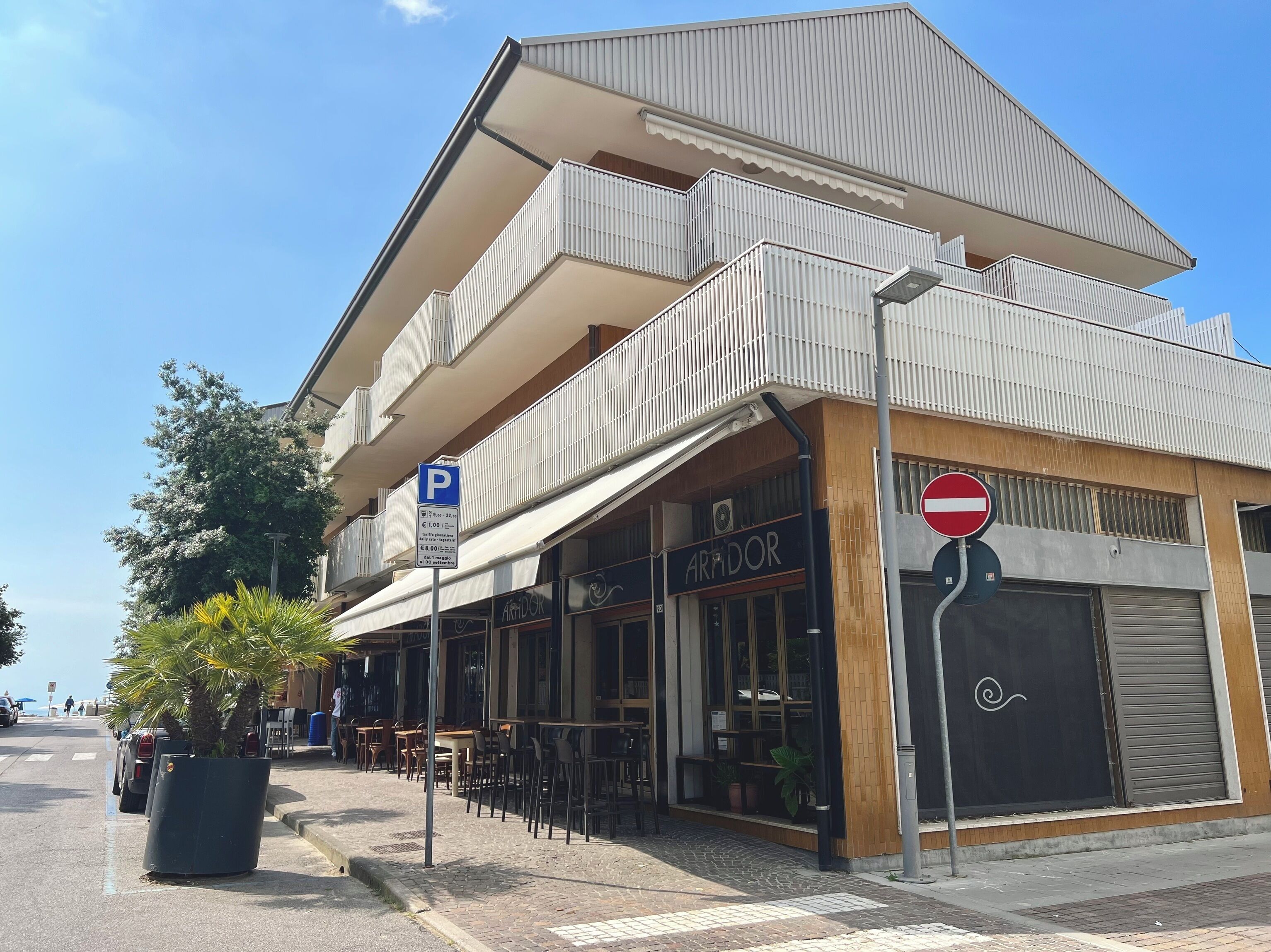 A building with a restaurant named 'ARIDOR' on the ground floor, a parking sign, and a no entry sign.
