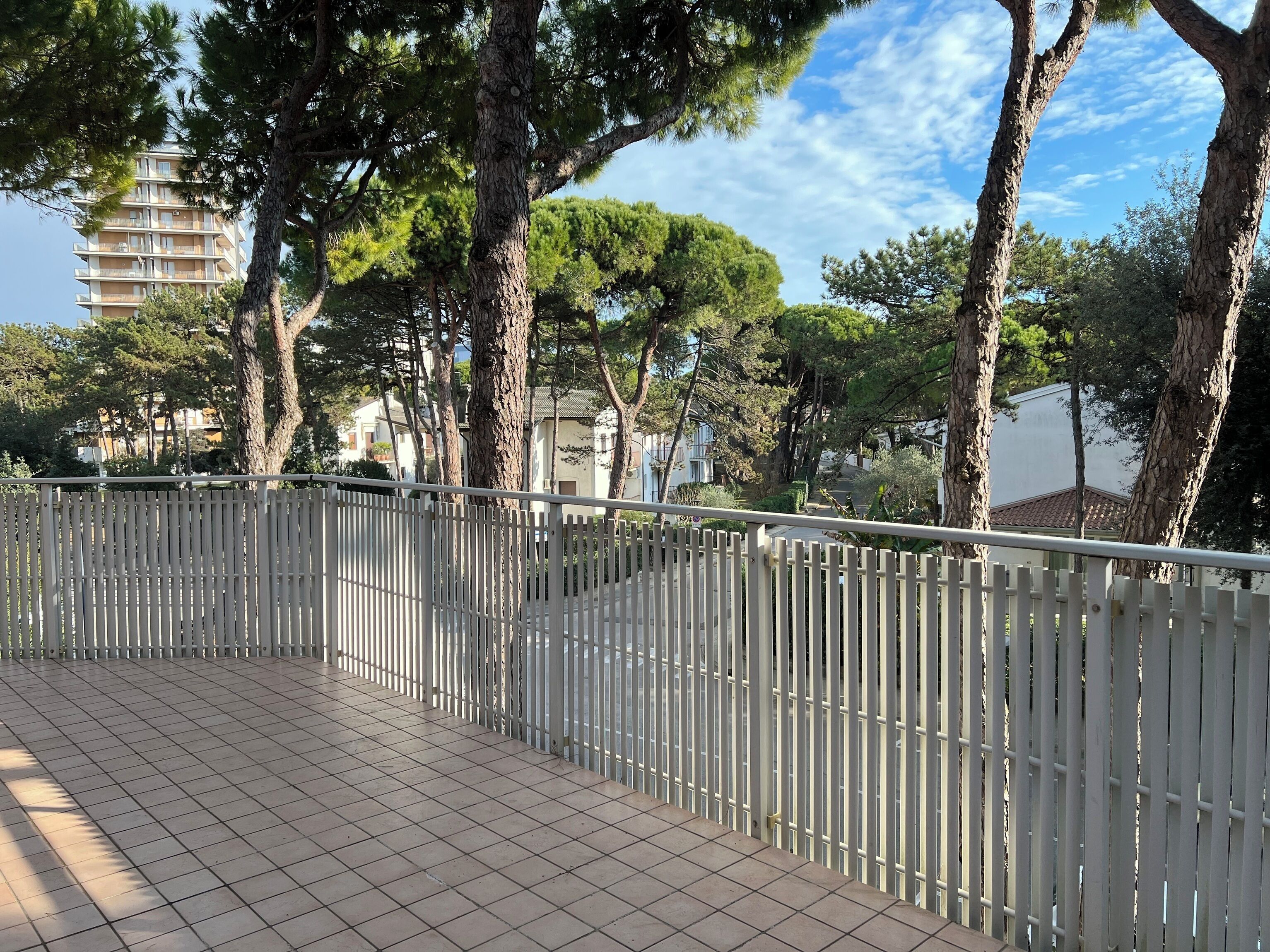 A tiled outdoor area with a white metal fence, trees, and residential buildings in the background.