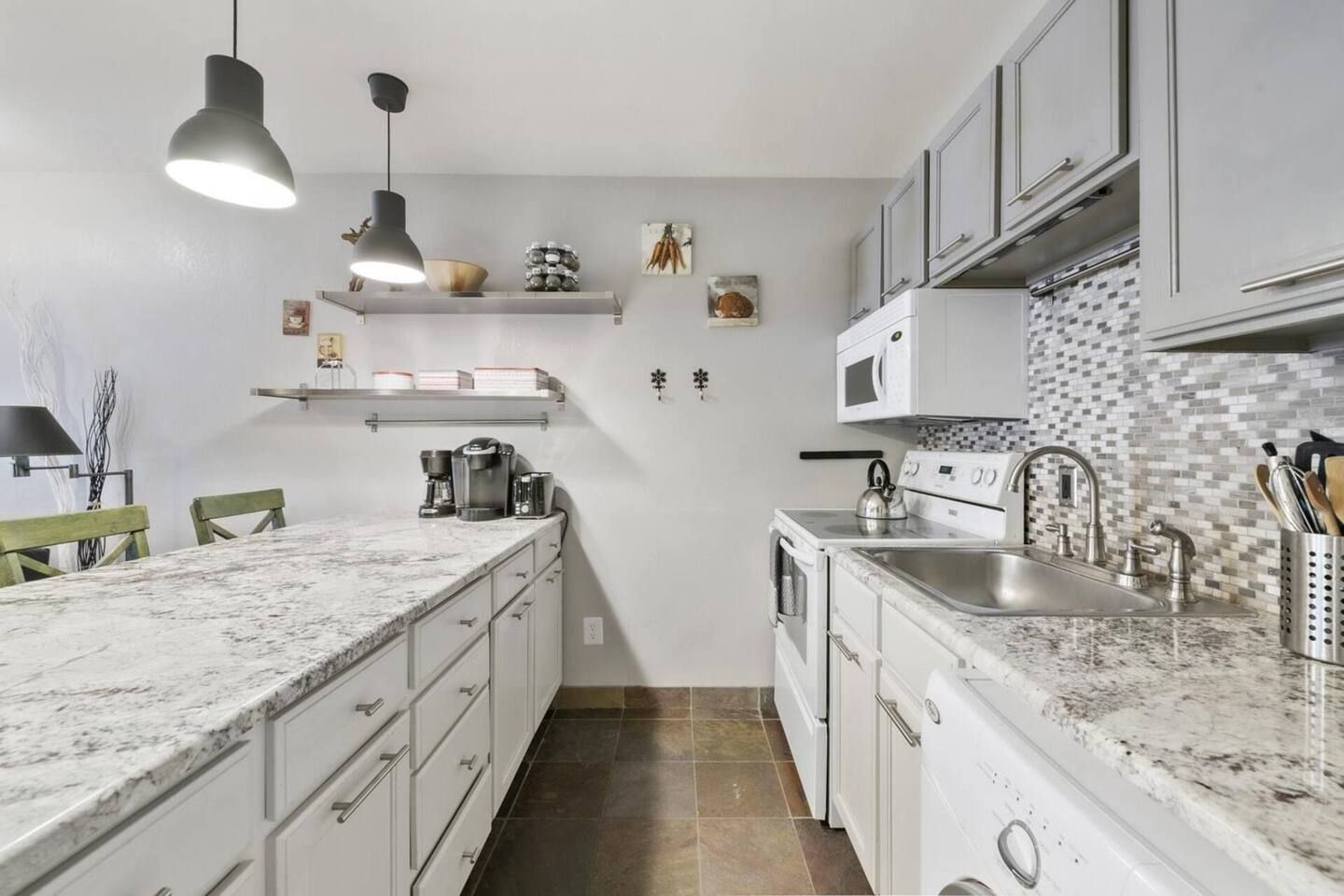A kitchen with white cabinets, a marble countertop, a built-in oven, a microwave, and a sink.