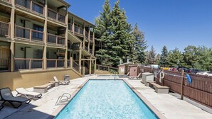 A rectangular pool with a wooden deck, lounge chairs, and a multi-story building with balconies. - Park City Snowcrest Chalet (Park City)