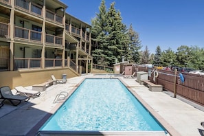 A rectangular pool with a wooden deck, lounge chairs, and a multi-story building with balconies. - Park City Snowcrest Chalet (Park City)