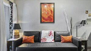 A modern living room with a black leather sofa, two orange cushions, a decorative pillow with the Eiffel Tower, a black floor lamp, and a framed abstract painting. - Park City Snowcrest Chalet (Park City)